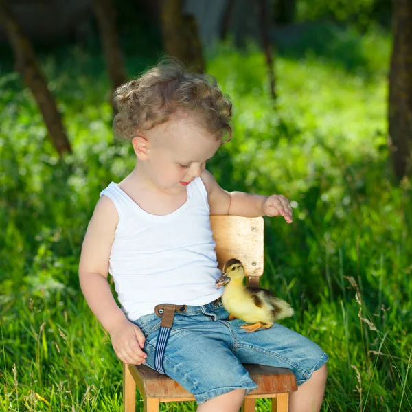 Menino com pouco patinho amarelo na aldeia de verão — Fotografia de Stock