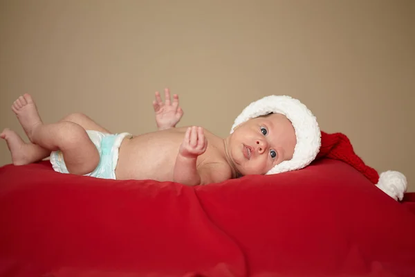 Bébé mignon avec chapeau de père Noël sur fond rouge — Photo