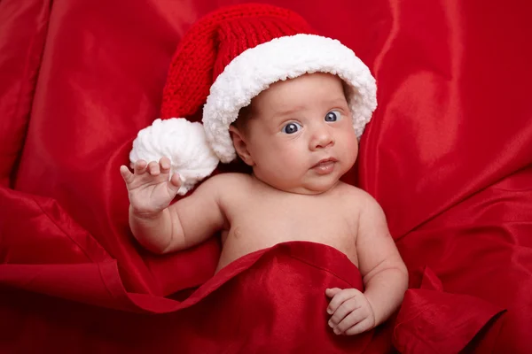 Niedliches Baby mit Weihnachtsmütze auf rotem Hintergrund — Stockfoto