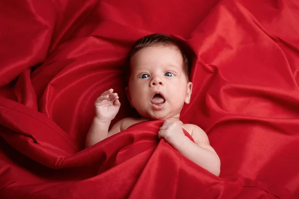 Lindo bebê deitado no fundo de seda vermelha — Fotografia de Stock