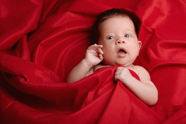 Schönes Baby auf rotem Seidenhintergrund liegend — Stockfoto