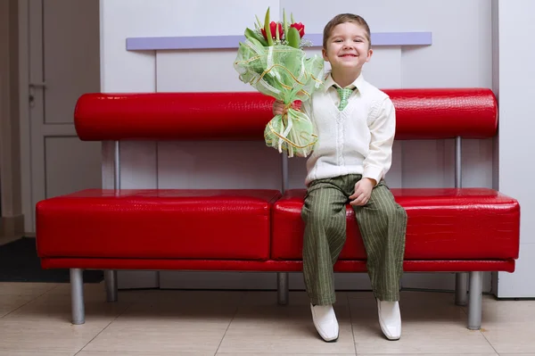 Pojken med blommor bukett sitter på soffan — Stockfoto