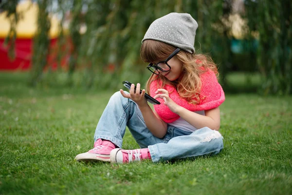 Niña con teléfono móvil en la hierba — Foto de Stock