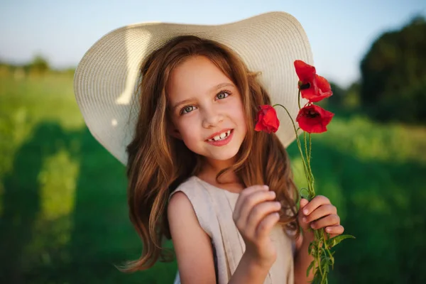 Gadis kecil yang lucu di padang rumput dengan bunga poppy merah Stok Foto