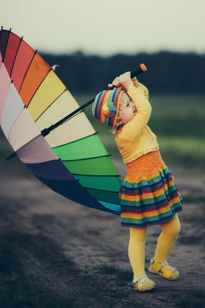 Kleines Mädchen mit Regenbogen-Regenschirm auf dem Feld — Stockfoto