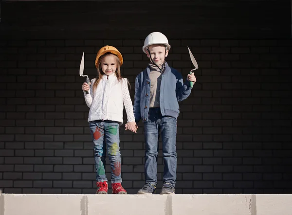 Little boy and girl in helmets build house — Stock Photo, Image