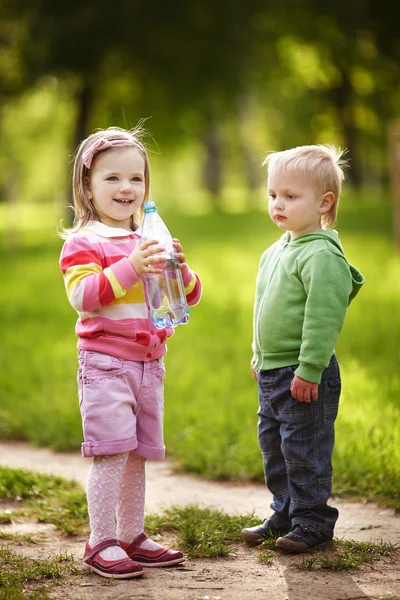 Niño y niña bebiendo agua mineral en el parque — Foto de Stock