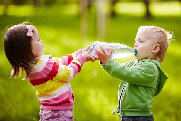 Девушка помогает мальчику держать бутылку — стоковое фото