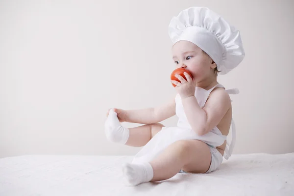 Cute little cook eats tomato — Stock Photo, Image
