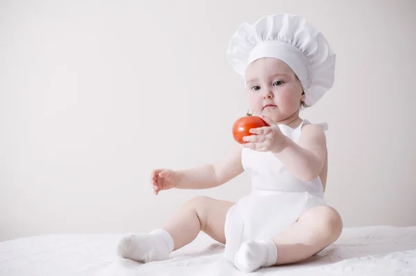 Cute little cook eats tomato — Stock Photo, Image