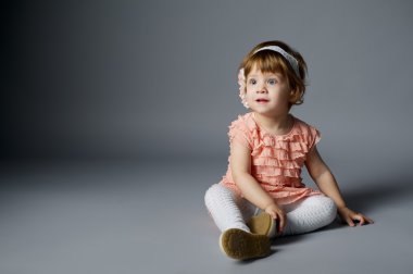 gri arka plan üzerinde oturan küçük kız