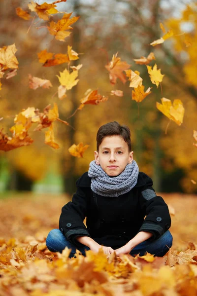 Niño sentado en hojas amarillas en el parque — Foto de Stock