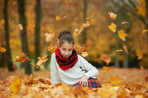 Chica sentada sobre hojas amarillas en el parque — Foto de Stock