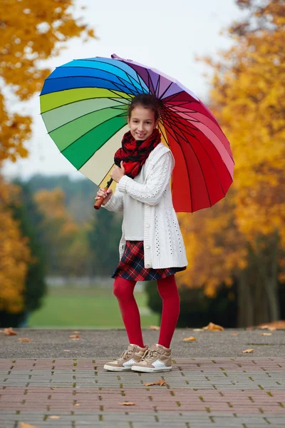 Menina sob guarda-chuva arco-íris no parque de outono — Fotografia de Stock