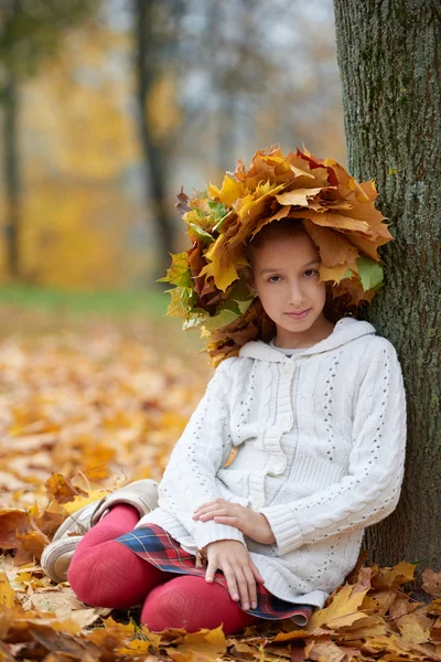 Vacker flicka i höst park med krans av löv — Stockfoto