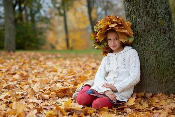 Schönes Mädchen im herbstlichen Park mit Laubkranz — Stockfoto