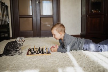 küçük çocuk yerde yatarken satranç oynar