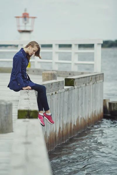 Prachtige blond meisje zit op pier — Stockfoto