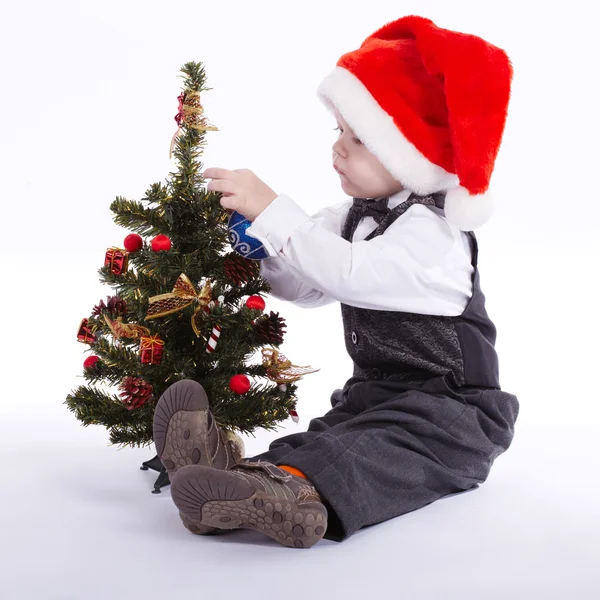 サンタの帽子を持つ少年がクリスマス ツリーを飾る — ストック写真