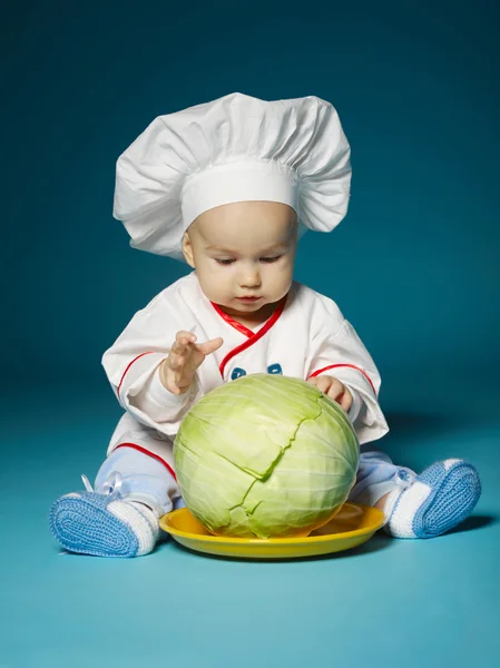 Bebê engraçado com traje de cozinheiro detém repolho — Fotografia de Stock