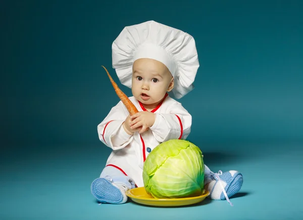 Funny baby with cook costume holds carrot — Stock Photo, Image