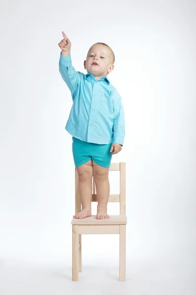 Niño en silla y apuntando con el dedo hacia arriba — Foto de Stock