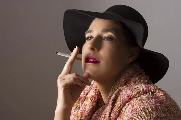 Mujer madura con sombrero negro sentarse a fumar — Foto de Stock