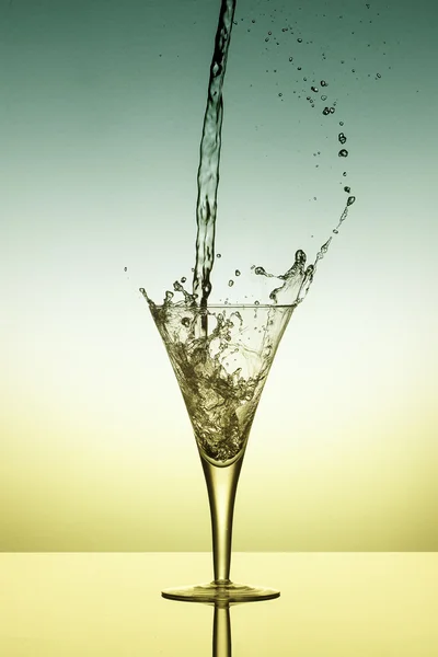 Water fall into a glass and splash on yellow and green backgroun — Stock Photo, Image