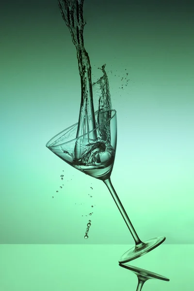 Water fall into a glass and splash on a green background — Stock Photo, Image