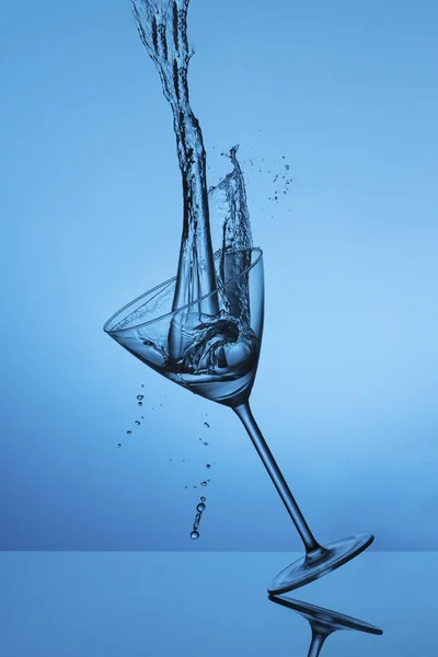 Water fall into a glass and splash on a blue background — Stock Photo, Image