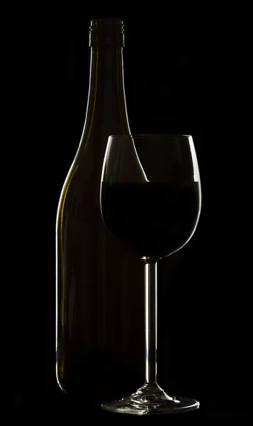 Glas wijn en een fles op zwarte achtergrond velg verlichting — Stockfoto