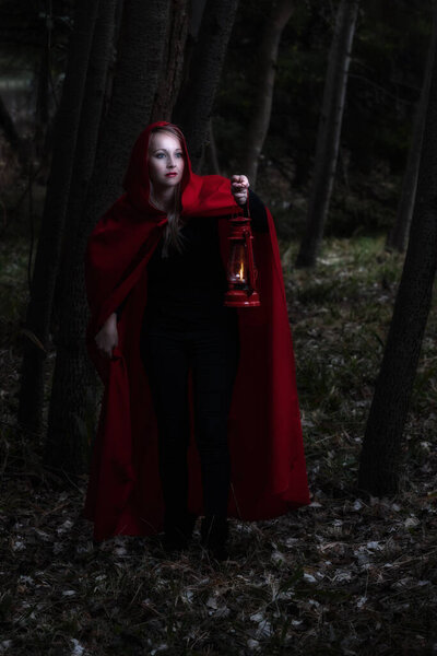 Attractive woman dressed a little red riding-hood walk in a dark forest with a lantern