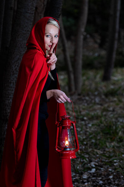 Attractive woman dressed a little red riding-hood walk in a dark forest with a lantern