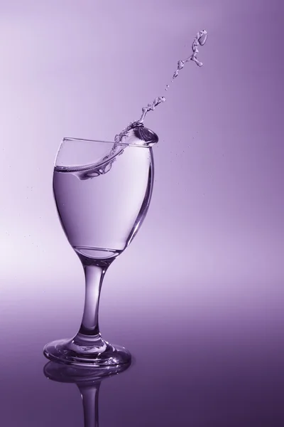 Glass with clear water falling over to spill with purple back li — Stock Photo, Image