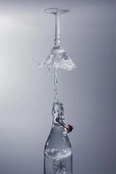 Чистая вода выливается из бутылки брызг в стекло с серой спиной — стоковое фото