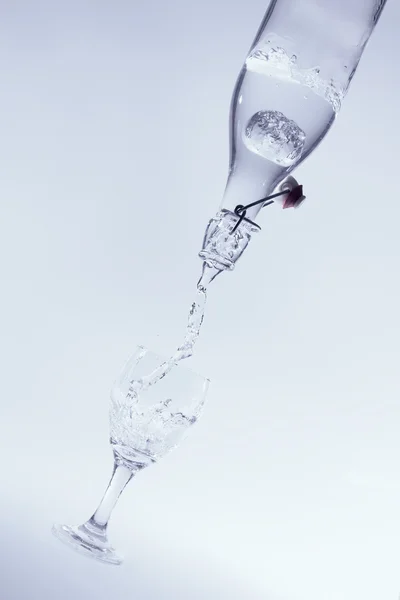 Wlać czystej wody z butelki rozchlapać do szkła z tyłu niebieski — Zdjęcie stockowe