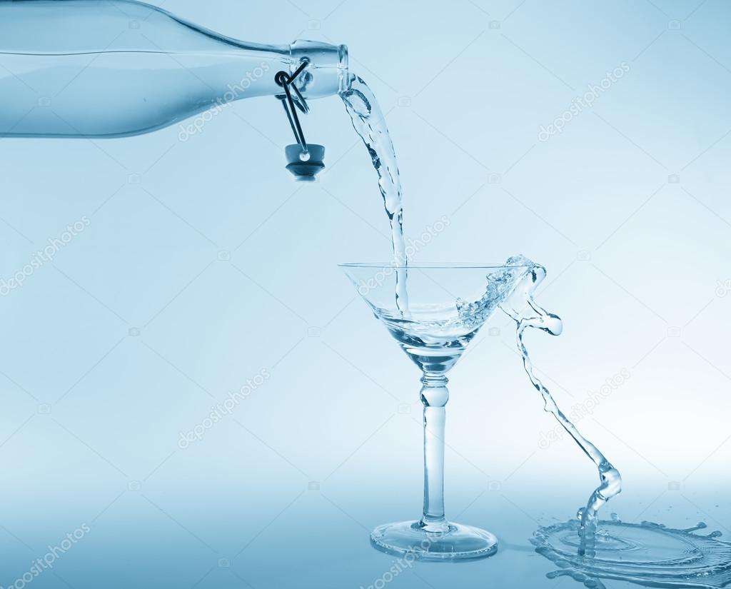Clear water pour out of bottle splash into glass and spill with 