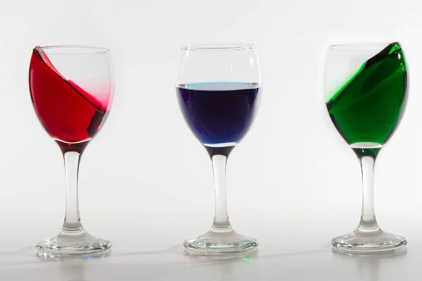 Três copos de vinho com derramamento de água a cores no fundo branco w — Fotografia de Stock