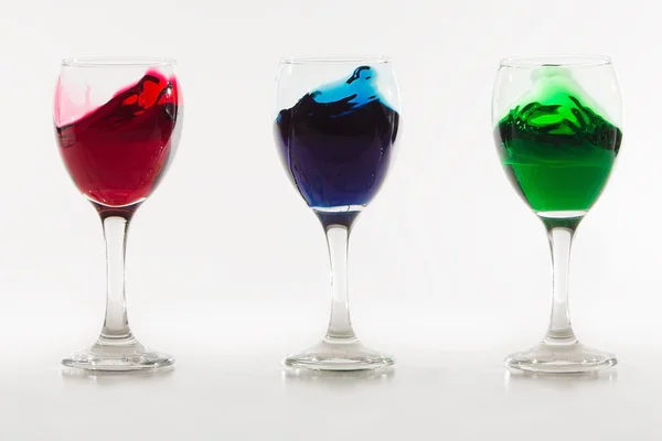 Três copos de vinho com derramamento de água a cores no fundo branco w — Fotografia de Stock