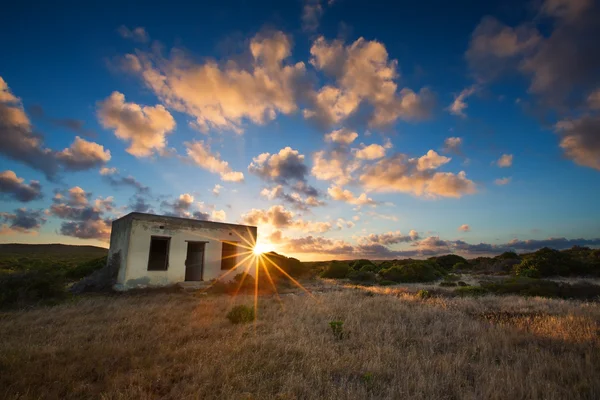 Старий маленький безлюдний будинок в полі з хмарним пейзажем заходу сонця — стокове фото