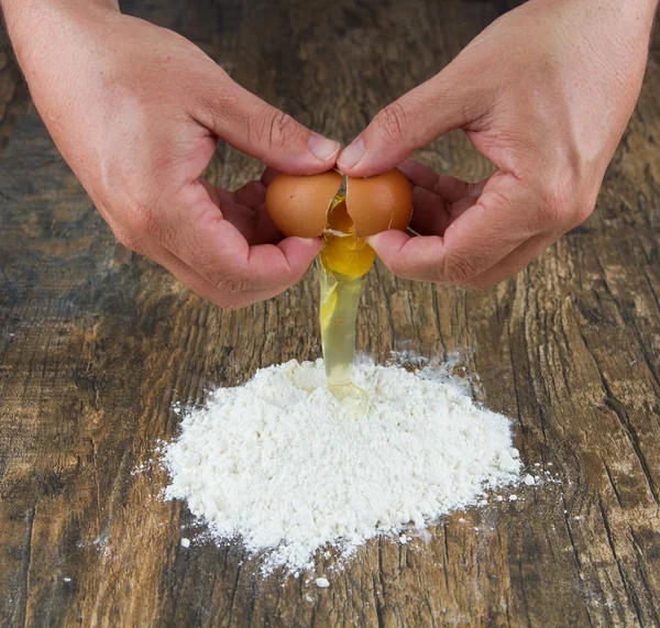 Two hands break egg on wooden surface on a heap of flour — Stock Photo, Image