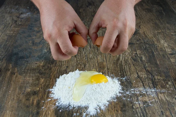 Two hands break egg on wooden surface on a heap of flour — Stock Photo, Image