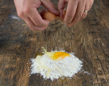 İki el bir yığın un üzerinde ahşap yüzey yumurta kırmak