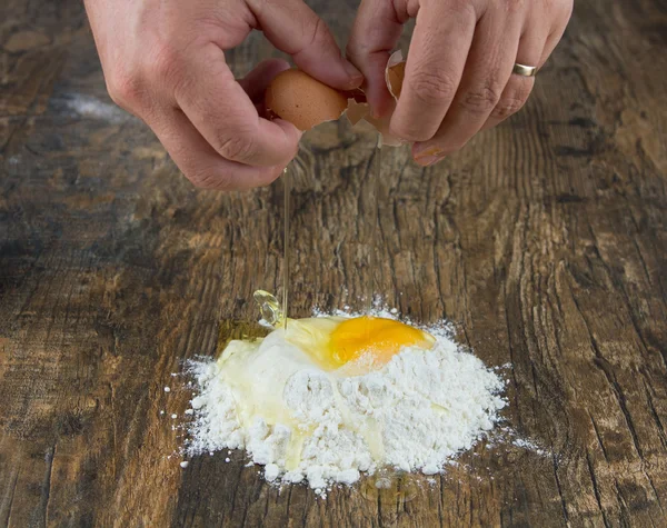 Two hands break egg on wooden surface on a heap of flour — Stock Photo, Image