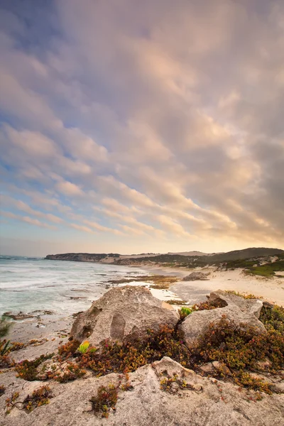 Landschap van de oceaan laat in de avond over rotsenstranden zware wolken bl Stockfoto