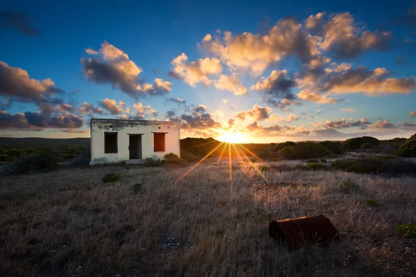 Старий маленький безлюдний будинок в полі з хмарним пейзажем заходу сонця — стокове фото