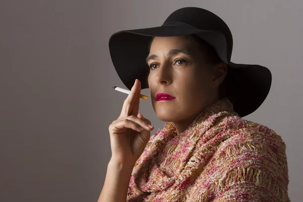 Mature woman with black hat sit smoking — Stock Photo, Image