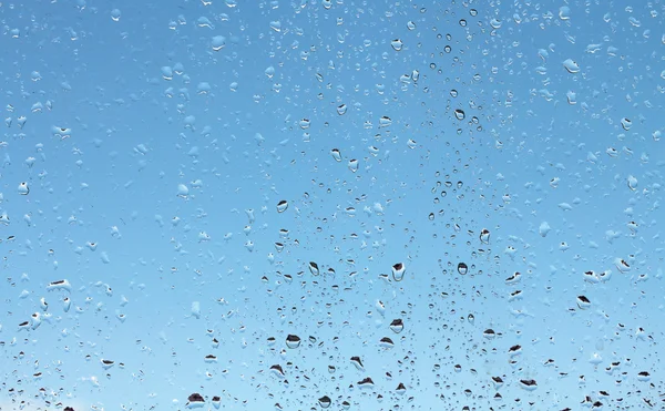 Gotas de agua sobre vidrio contra el cielo azul — Foto de Stock