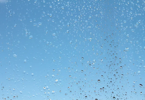 Gocce d'acqua su vetro contro cielo blu — Foto Stock