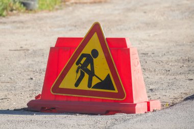 Bir adam yol tabelası üzerinde çalışıyor. İşaret kırmızı ve sarı ve elinde kürek olan siyah bir adam var.